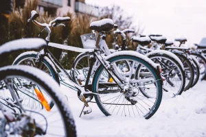 Mehrere Fahrräder stehen eingeschneit im Fahrradständer vor einer Schule.