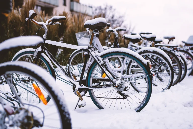 Mehrere Fahrräder stehen eingeschneit im Fahrradständer vor einer Schule.