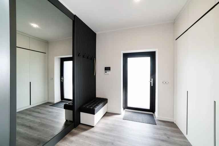 Heller moderner Flur mit dunklen Gestaltungselementen und einem großen Ganzkörperspiegel an der Wand.