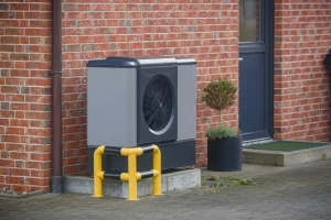 Eine Wärmepumpe neben dem Eingang eines Altbaus, dessen Fassade aus roten Backsteinen besteht.