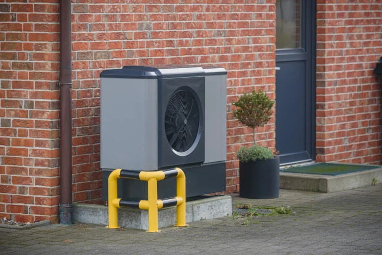 Eine Wärmepumpe neben dem Eingang eines Altbaus, dessen Fassade aus roten Backsteinen besteht.