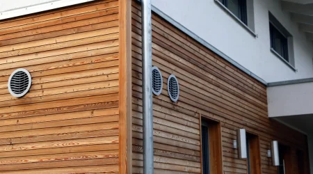 Fassade mit moderner horizontaler Holzverkleidung, kombiniert mit weißen Putzflächen und runden Lüftungsgittern.