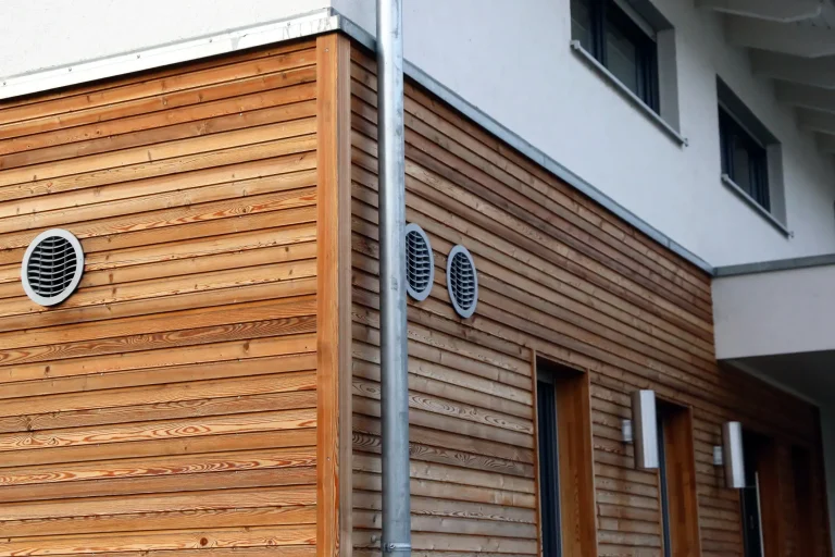 Fassade mit moderner horizontaler Holzverkleidung, kombiniert mit weißen Putzflächen und runden Lüftungsgittern.