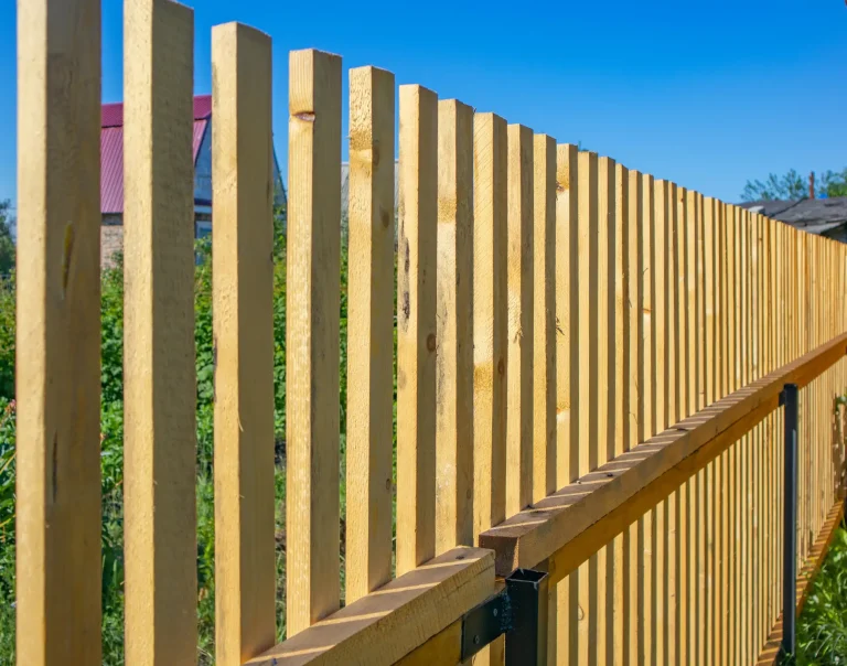 Moderner Holzzaun aus senkrechten Holzlatten mit Metallverstärkung, aufgenommen bei blauem Himmel.