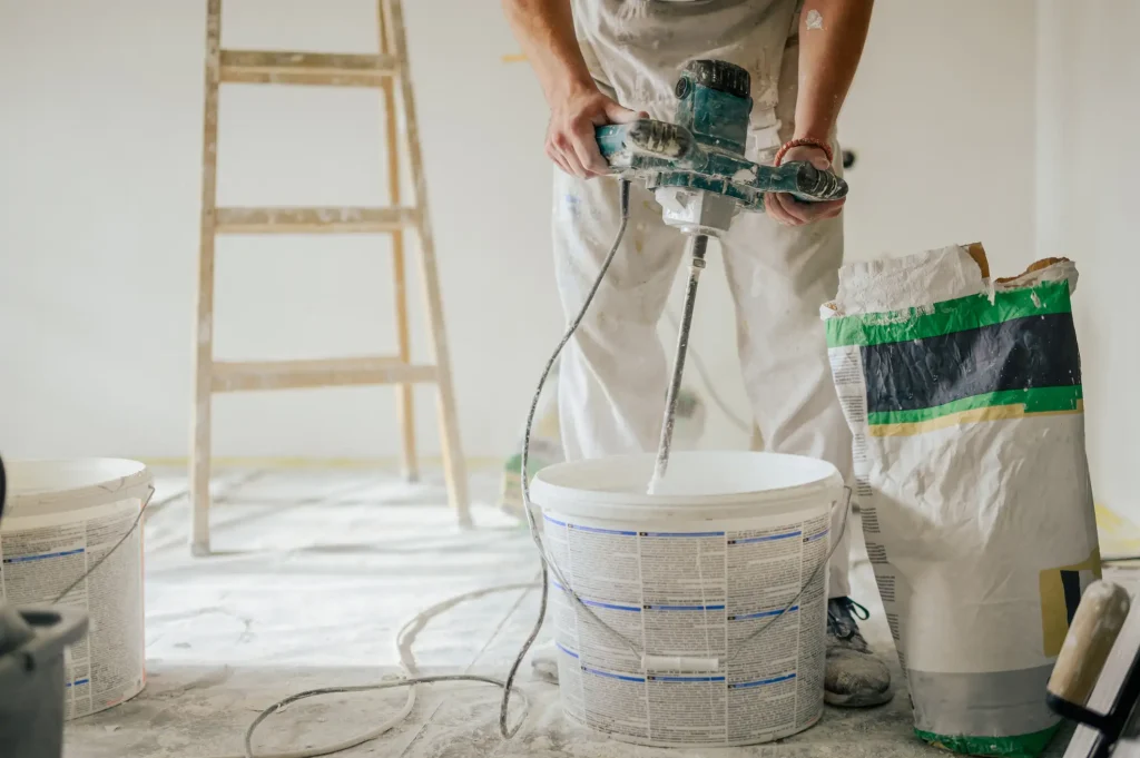 Handwerker rührt Kalkputz mit einem elektrischen Rührgerät in einem Eimer an.