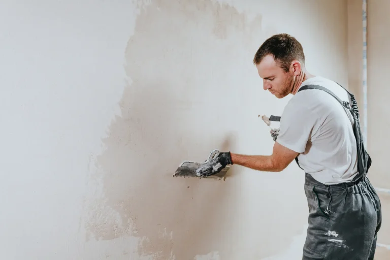 Maler trägt Kalkputz mit einer Kelle auf eine Innenwand auf.