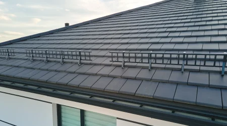 Professionell montiertes Schneefangsystem mit grauen Schneefanggittern auf einem neu eingedeckten Dach mit modernen, flachen Dachziegeln in Anthrazit. Das System schützt effektiv vor Dachlawinen.