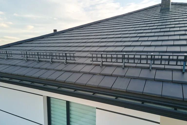 Professionell montiertes Schneefangsystem mit grauen Schneefanggittern auf einem neu eingedeckten Dach mit modernen, flachen Dachziegeln in Anthrazit. Das System schützt effektiv vor Dachlawinen.