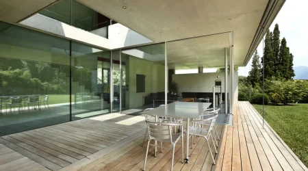 Moderne Terrasse mit Glasverglasung, großen Schiebetüren und Holzfußboden, Blick ins Wohnzimmer und Garten.