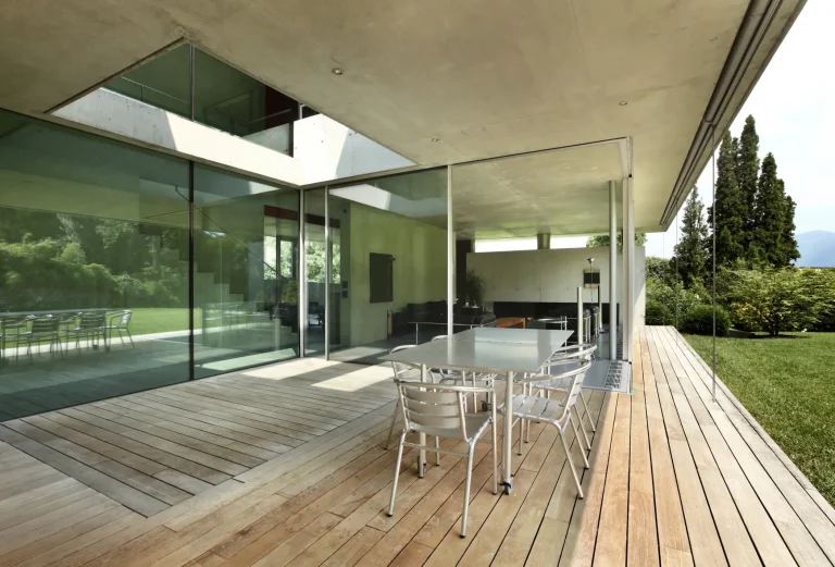 Moderne Terrasse mit Glasverglasung, großen Schiebetüren und Holzfußboden, Blick ins Wohnzimmer und Garten.