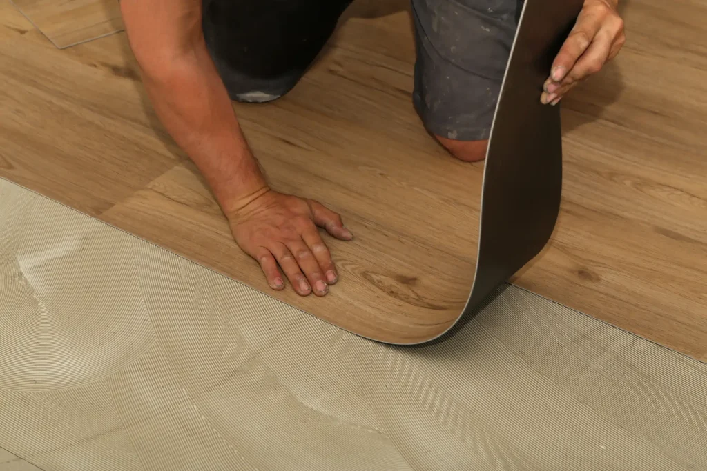 Handwerker verlegt Vinylboden in Holzoptik auf vorbereiteten Untergrund mit Kleber.