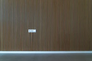 Moderne Innenwandverkleidung aus vertikalen Holzlatten in einem minimalistischen Raum, mit sichtbaren Steckdosen und Lichtschalter.