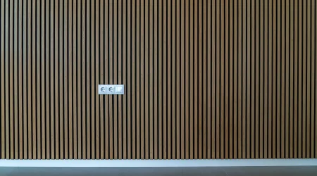 Moderne Innenwandverkleidung aus vertikalen Holzlatten in einem minimalistischen Raum, mit sichtbaren Steckdosen und Lichtschalter.