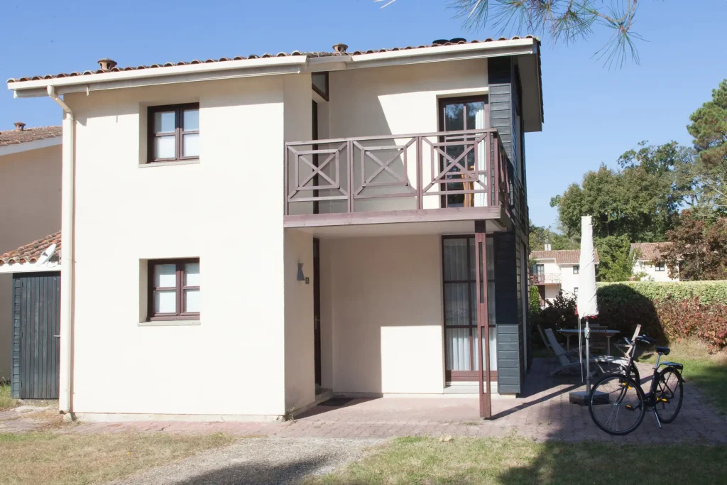 Modernes Einfamilienhaus mit einem Anbaubalkon aus Holz und Metallgeländer, der über einer überdachten Terrasse angebracht ist.