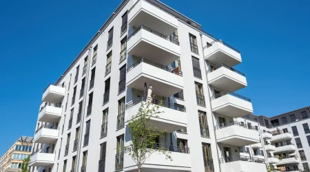 Modernes Mehrfamilienhaus mit mehreren über Eck angeordneten Balkonen, hellen Fassaden und klarer, zeitgenössischer Architektur.