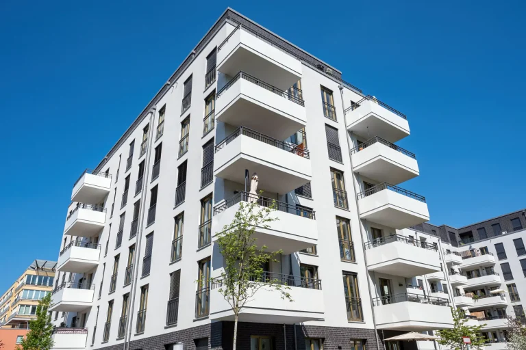 Modernes Mehrfamilienhaus mit mehreren über Eck angeordneten Balkonen, hellen Fassaden und klarer, zeitgenössischer Architektur.