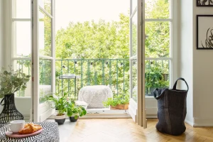 Heller französischer Balkon mit geöffneten Doppeltüren, vielen grünen Pflanzen und gemütlicher Sitzgelegenheit im modernen Wohnstil.