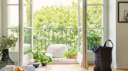 Heller französischer Balkon mit geöffneten Doppeltüren, vielen grünen Pflanzen und gemütlicher Sitzgelegenheit im modernen Wohnstil.