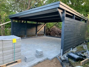 Teilweise fertiggestellter Carport mit grauen Pflastersteinen und dunkler Holzverkleidung