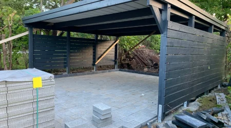 Teilweise fertiggestellter Carport mit grauen Pflastersteinen und dunkler Holzverkleidung