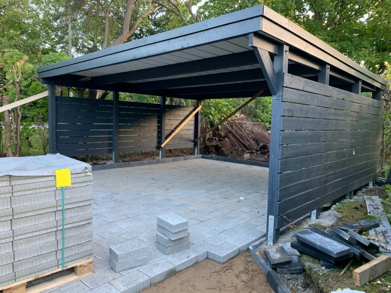 Teilweise fertiggestellter Carport mit grauen Pflastersteinen und dunkler Holzverkleidung