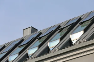 Schrägdach mit mehreren modernen Dachfenstern und grauer Metallverkleidung unter blauem Himmel