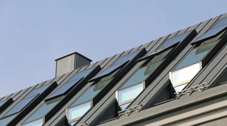 Schrägdach mit mehreren modernen Dachfenstern und grauer Metallverkleidung unter blauem Himmel