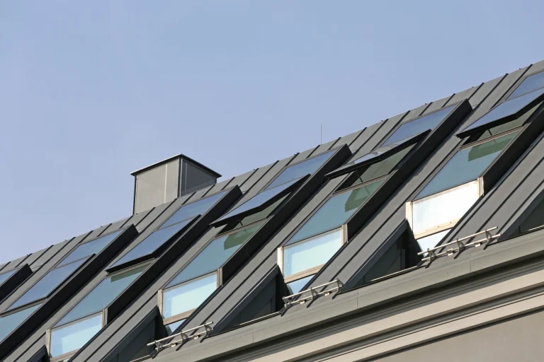 Schrägdach mit mehreren modernen Dachfenstern und grauer Metallverkleidung unter blauem Himmel