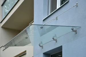Modernes Glasvordach mit Edelstahlhaltern und Spannseilen an einer Hausfassade, das den Eingangsbereich vor Regen schützt.