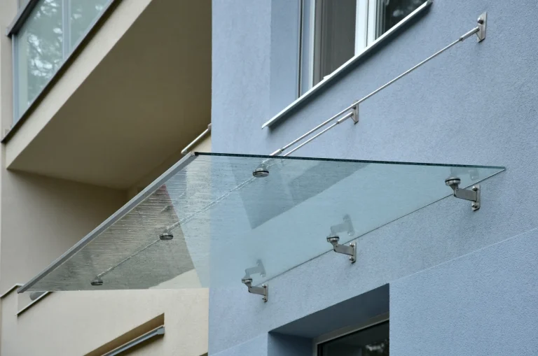 Modernes Glasvordach mit Edelstahlhaltern und Spannseilen an einer Hausfassade, das den Eingangsbereich vor Regen schützt.