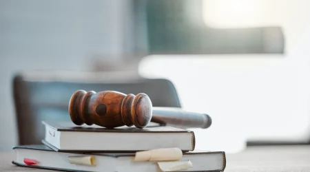 Ein Richterhammer liegt auf einem Stapel Bücher, auf einem Konferenztisch.