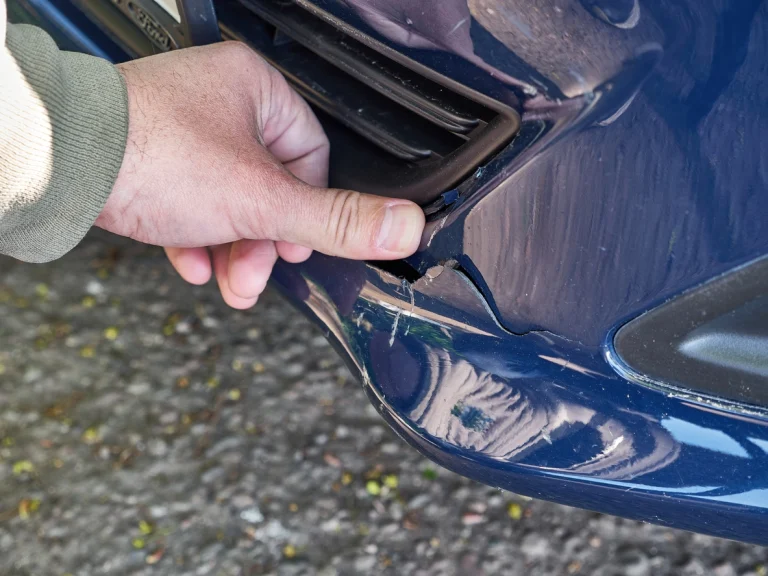 Eine Person begutachtet den Schaden an der Stoßstange des Autos.