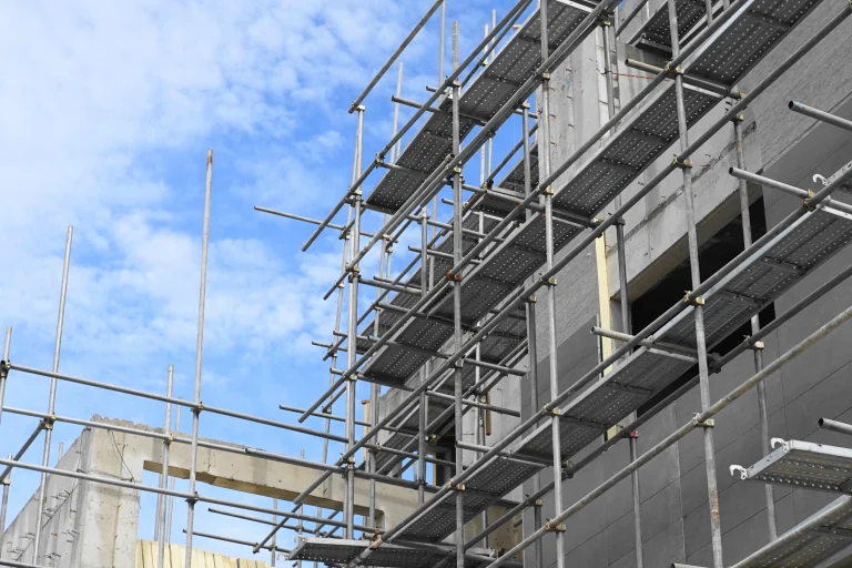 Ein Baugerüst an einer grauen unverputzten Außenfassade eines Neubaus.