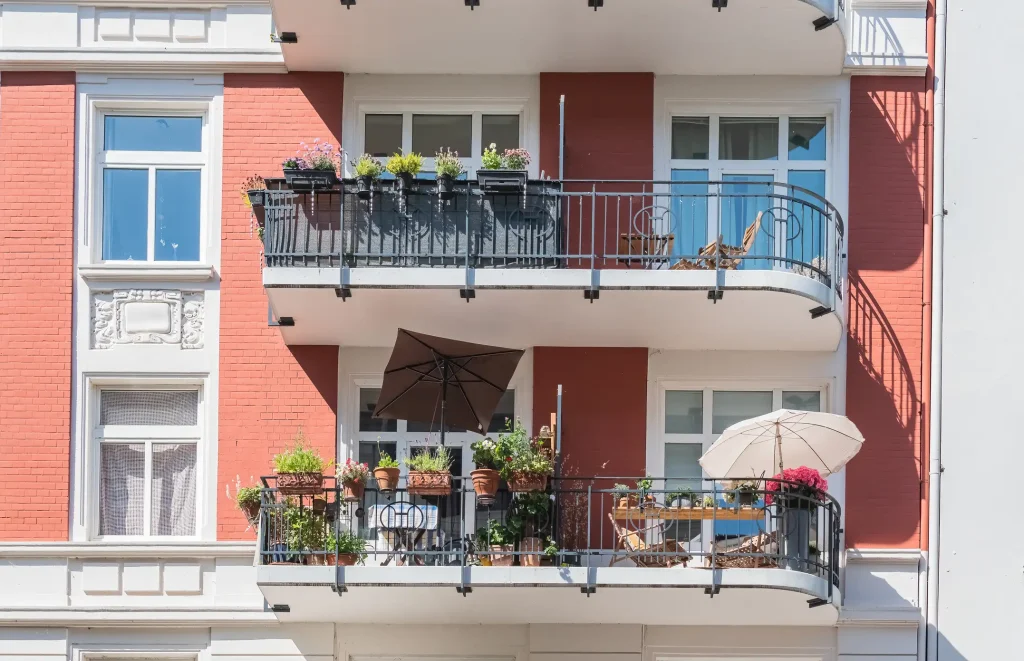 Fassade eines Mehrfamilienhauses mit mehreren bepflanzten Kragarmbalkons mit schwarzen Geländern, Sonnenschirmen und Sitzmöbeln.