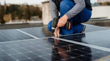 Person installiert Solarmodule auf einem Dach mit Akkuschrauber