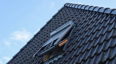 Schrägdach mit geöffnetem Dachfenster und dunklen Dachziegeln unter blauem Himmel