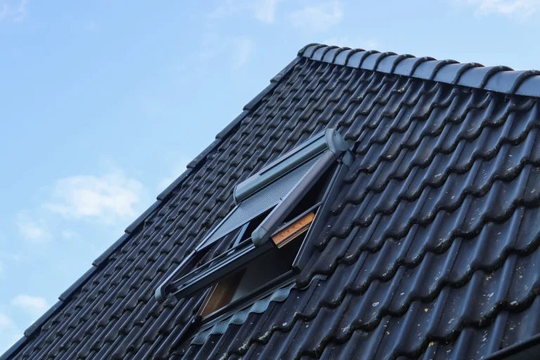 Schrägdach mit geöffnetem Dachfenster und dunklen Dachziegeln unter blauem Himmel