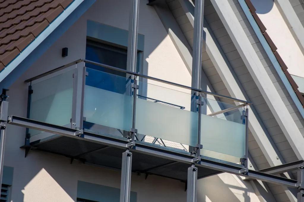 Moderner Vorstellbalkon aus Stahl mit Milchglasbrüstung an einem Wohnhaus mit Satteldach und großen Fensterflächen.