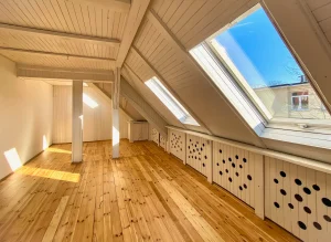 Helles ausgebaute Dachgeschoss mit aufbereiteten Holzdielen und großen Dachfenstern, durch die Sonnenlicht einfällt.