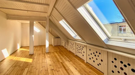 Helles ausgebaute Dachgeschoss mit aufbereiteten Holzdielen und großen Dachfenstern, durch die Sonnenlicht einfällt.