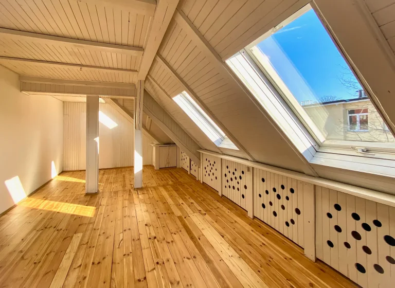 Helles ausgebaute Dachgeschoss mit aufbereiteten Holzdielen und großen Dachfenstern, durch die Sonnenlicht einfällt.