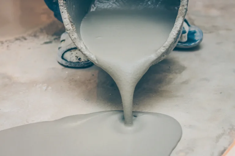 Frisch angerührter Estrich wird aus einem Eimer auf den Boden gegossen, dabei wird die Feuchtigkeit des Materials während des Bauprozesses kontrolliert.