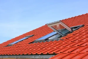 Rotes Ziegeldach mit mehreren Hochschwingfenstern, von denen eines geöffnet ist und Licht sowie frische Luft in den Dachraum lässt.