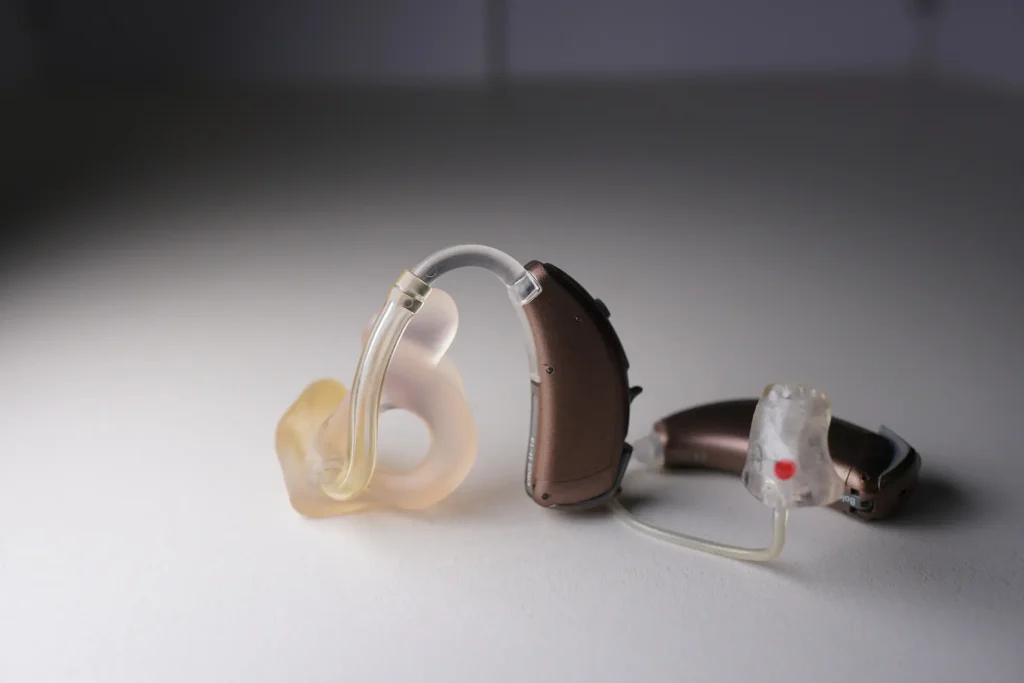 Modernes Hörgerät mit individuell angefertigter Otoplastik liegt auf einer hellen Fläche. Das Hörgerät zeigt den Schallschlauch und die angepasste Ohrpassform deutlich.