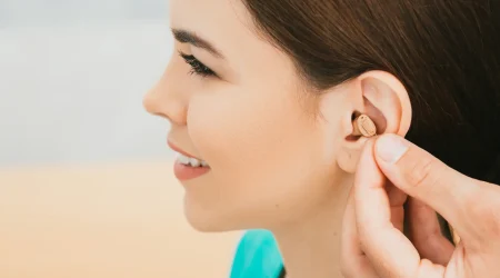 Hörakustiker setzt ein dezentes Im-Ohr-Hörgerät bei einer jungen Frau ein.