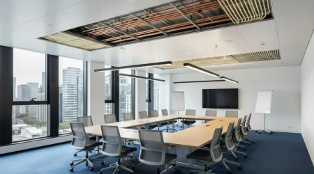 Modernes Büro mit geöffneter Deckenkonstruktion, sichtbar verlegten Leitungen und Kühlregister einer Kühldecke über einem großen Konferenztisch.