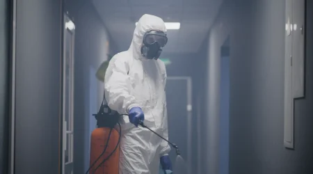 Ein Tatortreiniger in Schutzanzug, Atemmaske und Handschuhen führt in einem Gebäude im Rahmen einer professionellen Tatortreinigung eine Luftdesinfektion durch.