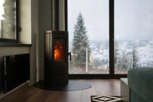 Raumluftabhängiger Kaminofen in einem Wohnzimmer mit Blick auf verschneite Landschaft, der Raumluft zur Verbrennung nutzt und Wärme in den Raum abgibt.