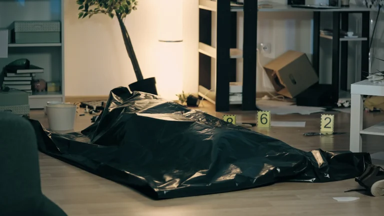 Ein Tatort mit einer abgedeckten Leiche auf dem Boden und nummerierten Markierungen, wie sie bei Ermittlungen üblich sind, bevor eine Raumluftdesinfektion und Reinigung des Fundortes erfolgt.