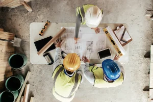 Drei Handwerker aus Vogelperspektive auf einer Baustelle, stehen um einen Tisch herum und planen den weiteren Verlauf.